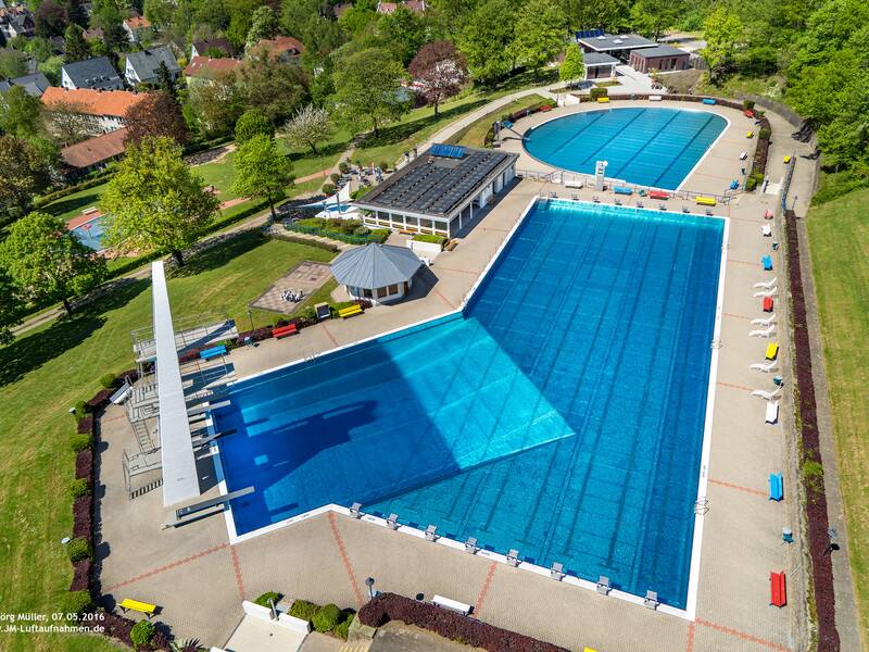 Die Luftaufnahme zeigt das Bergbad, ein großes Freibad mit mehreren Schwimmbecken, von Bäumen umgeben.