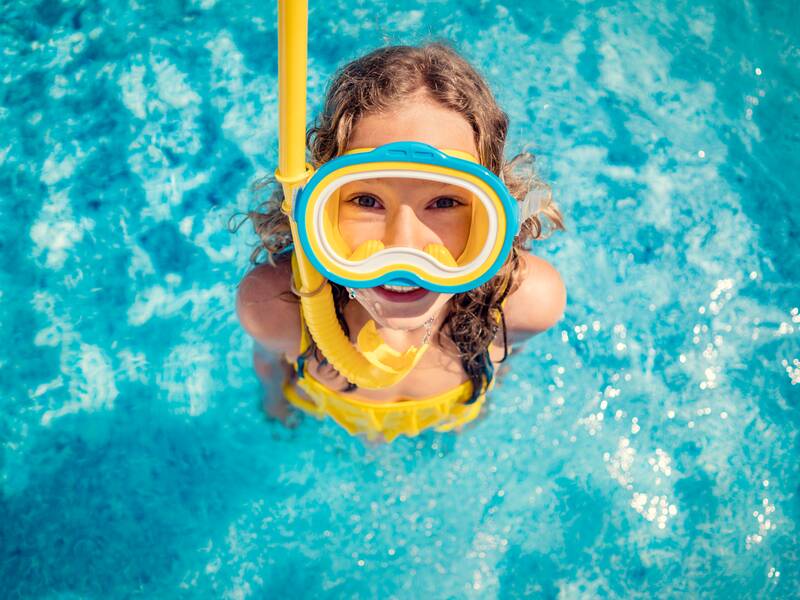 Kind mit Taucherbrille steht im Schwimmbecken