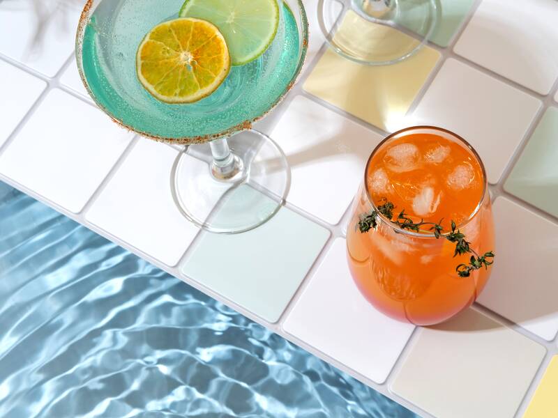 Drei bunte Cocktails stehen am Rand eines Schwimmbeckens