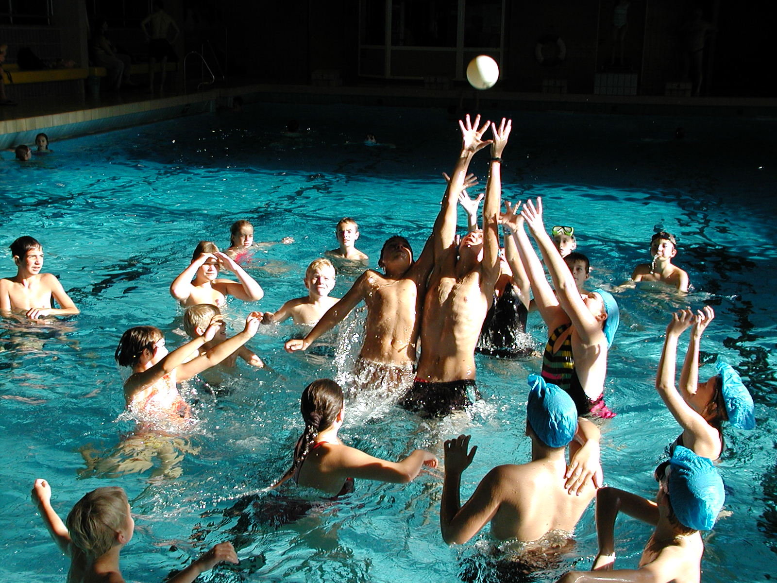 Eine Gruppe von Kindern spielt im Hallenbad, wobei einige nach einem Ball greifen.